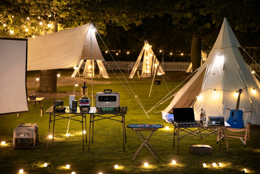 Portable power station charging laptop and smartphone at a modern campsite with ambient lighting