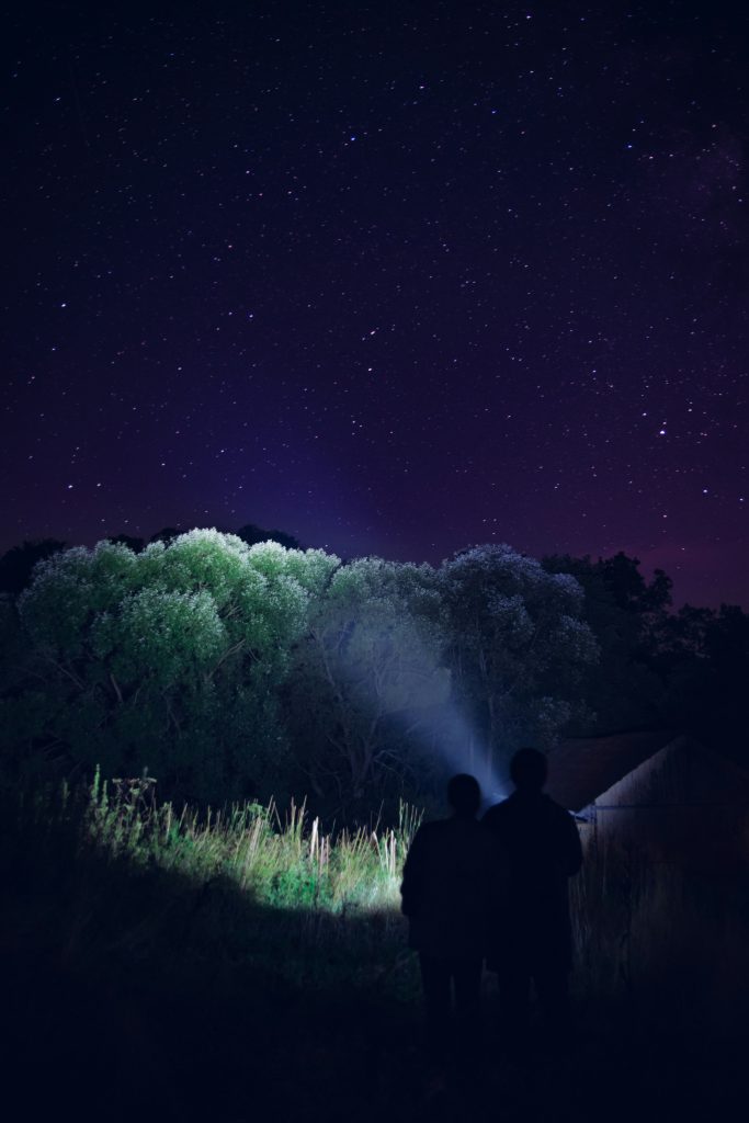 Outdoor enthusiast using advanced headlamp while setting up tent in dark forest with ambient campsite lighting