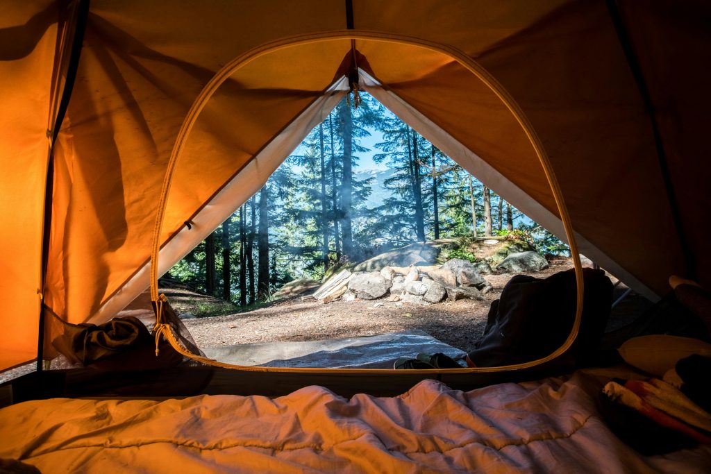 View from inside a tent showing cozy sleeping bag, backpack, and campfire smoke outside amidst pine forest - inspiring durable outdoor furniture for backyard relaxation